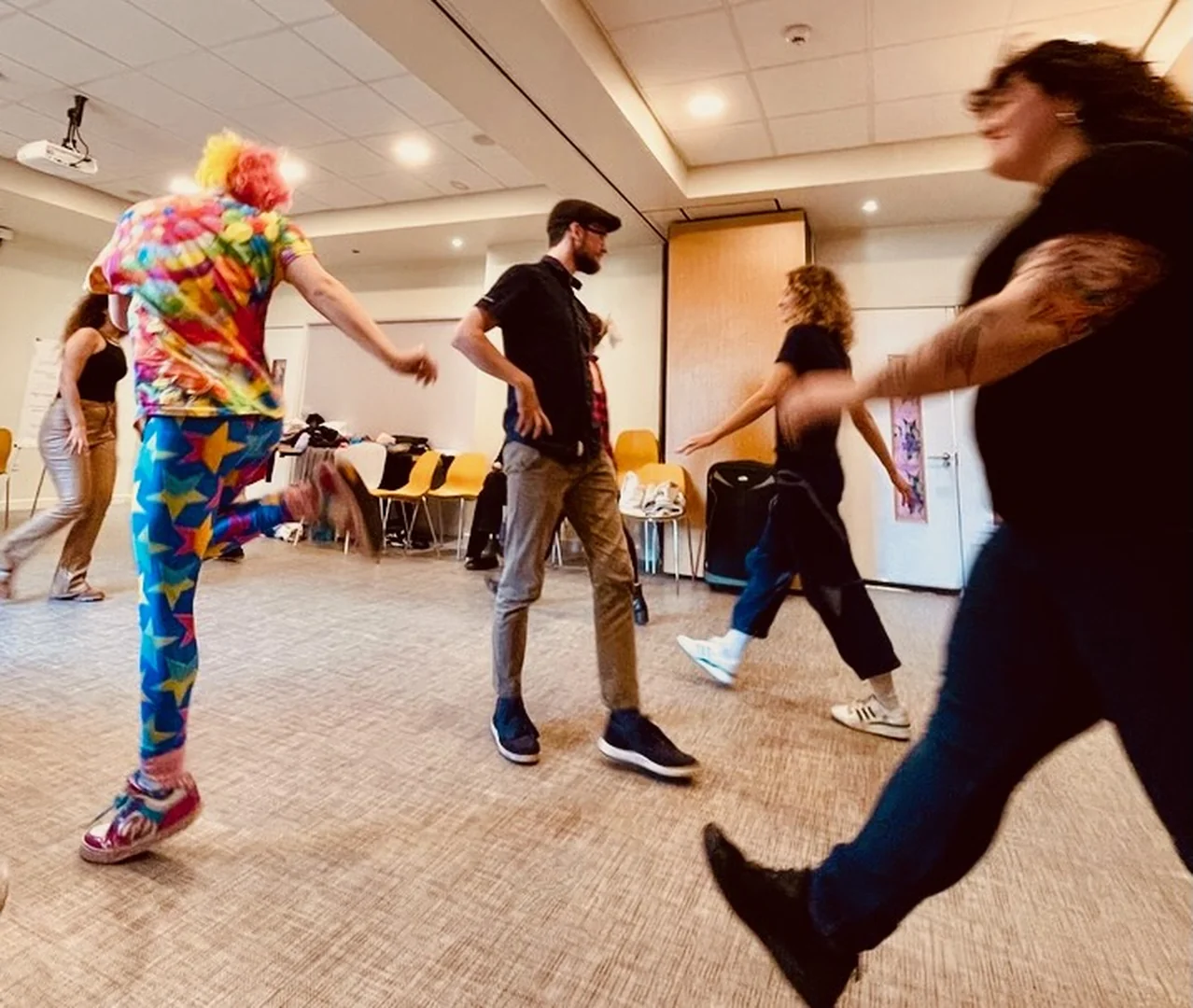Participants move through a bright room during a playful workshop exercise, with chairs along the back wall.